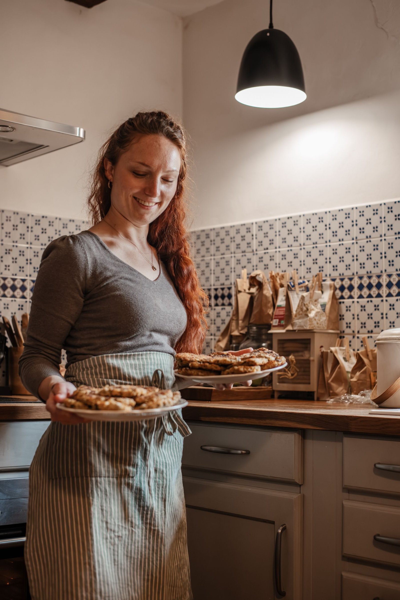 Laura Bridier dans sa cuisine, souriante, deux plats de tartes dans les mains.
