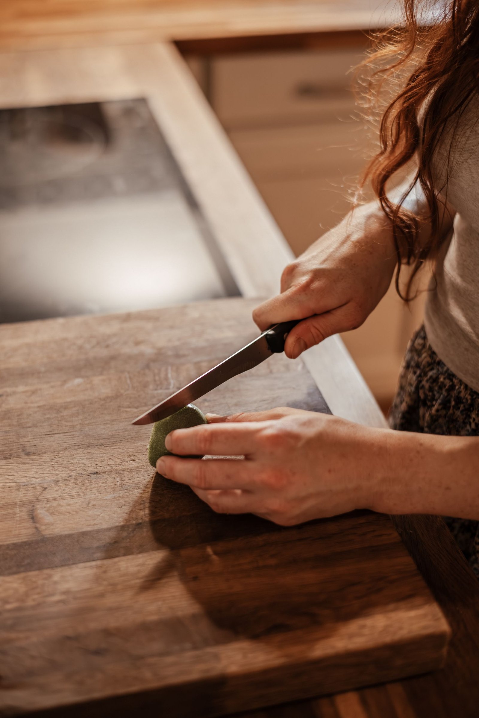 Mains de Laura découpant un légume sur une planche de bois.