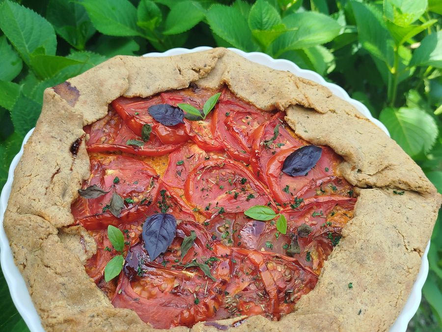 Tarte rustique aux tomates et au basilic, pâte au sarrasin, posée dans les feuillages.