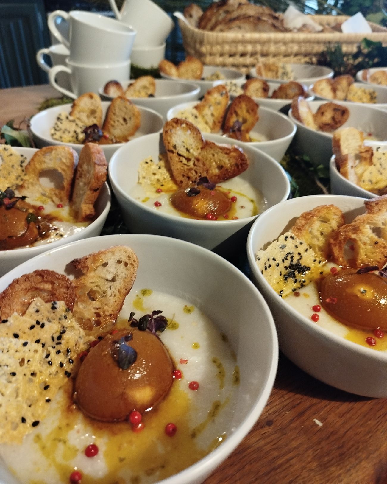 Bols dressés en série pour un brunch : crème, fruit poché, baies roses et pain grillé.