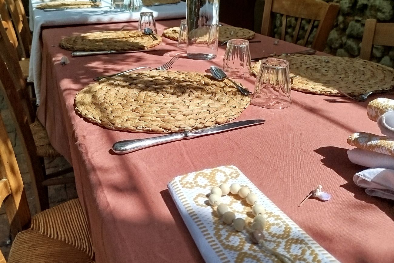Longue tablée dressée dans une cour de pierre, nappe rose et sets tressés.