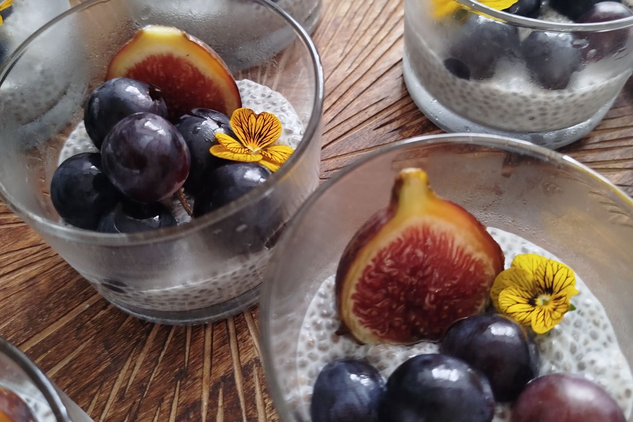 Coupes de pudding de chia garnies de figues, de prunes et de fleurs comestibles.