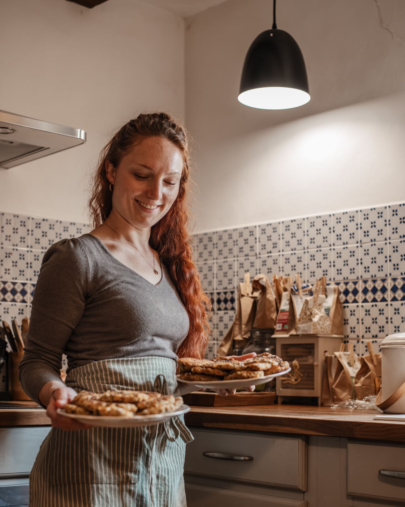 Laura Bridier dans sa cuisine, souriante, deux plats de tartes dans les mains.