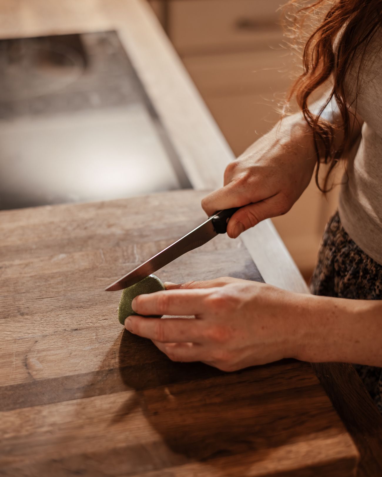 Mains de Laura découpant un légume sur une planche de bois.